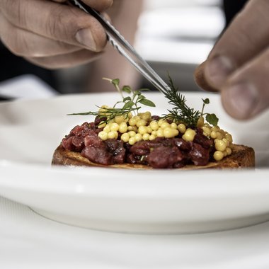 Aktivurlaub in Südtirol: ein Erlebnis Hände dekorieren ein Gericht mit frischen Kräutern und gelben Perlen