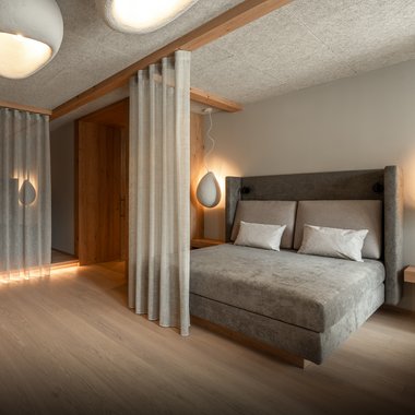Our hotel with gym in South Tyrol Modern bedroom with gray bed, curtains, and soft lighting