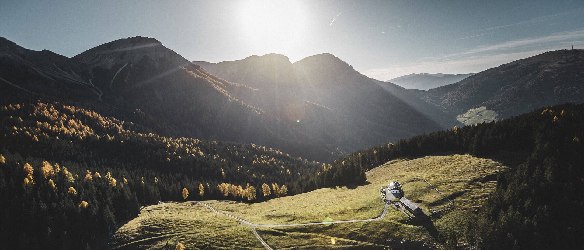 Das Wellnesshotel im Pustertal zum Entspannen Sonnenlicht über einer grünen Alm in den Bergen mit einem kleinen Haus