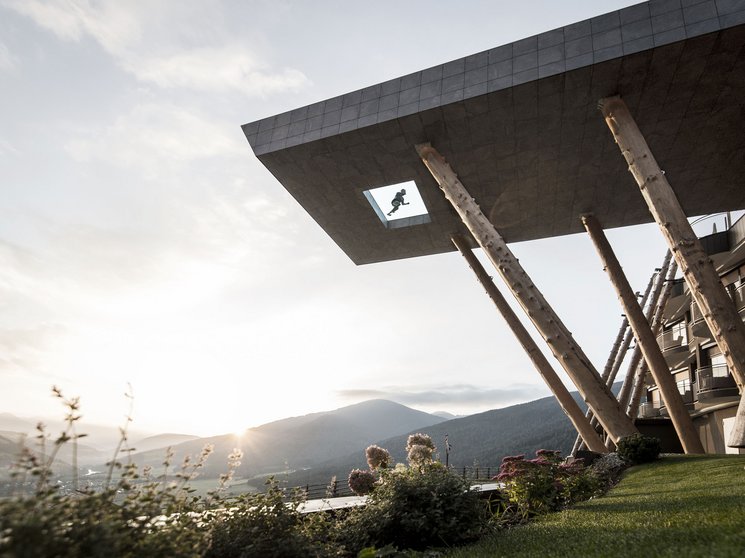 Das Wellnesshotel im Pustertal zum Entspannen Modernes Gebäude mit Holzstützen vor Berglandschaft bei Sonnenuntergang