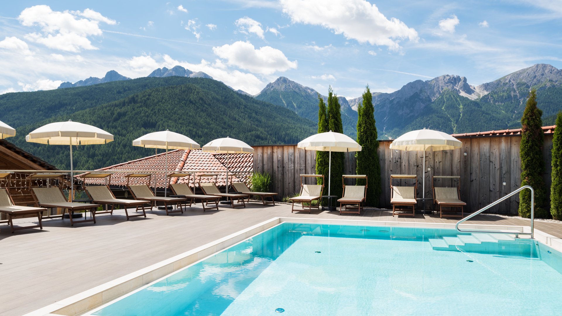 Il nostro hotel con infinity pool in Alto Adige: una meraviglia Area piscina con lettini, ombrelloni e montagne alpine sullo sfondo