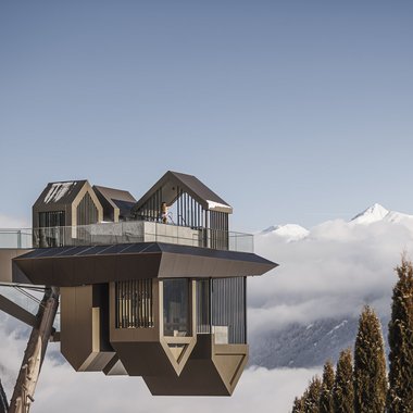 Awards & Press Moderne Bergstation über Bäumen mit schneebedeckten Gipfeln im Hintergrund