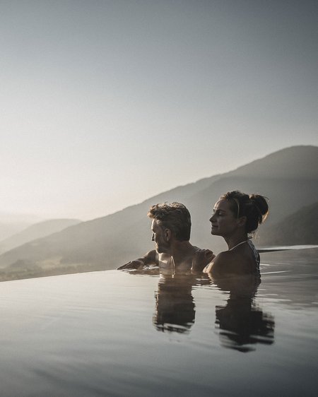 Our 5-star hotel in Italy between heaven and earth Couple relaxing in infinity pool overlooking mountains at sunset