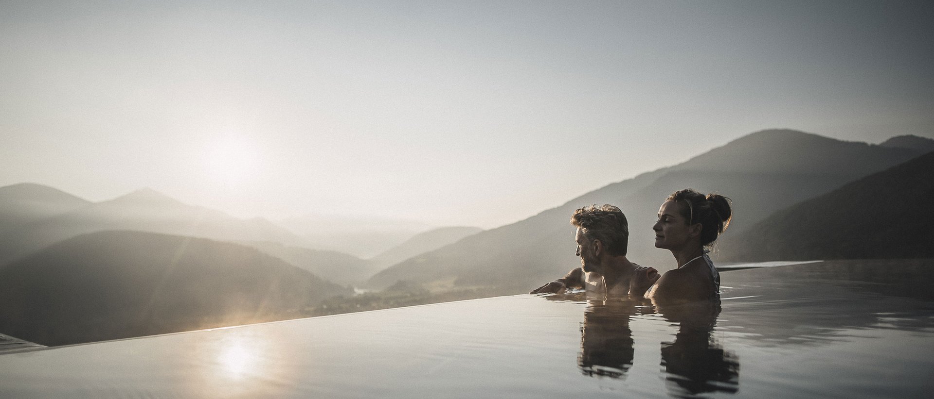 Unser Sky Pool in Südtirol, ein Prachtexemplar Paar entspannt in Infinity-Pool mit Bergblick bei Sonnenuntergang
