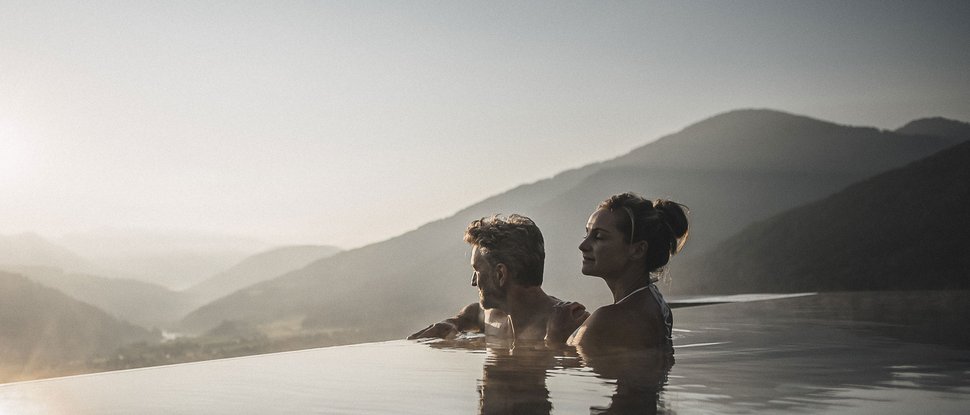 Our 5-star hotel in Italy between heaven and earth Couple relaxing in infinity pool overlooking mountains at sunset