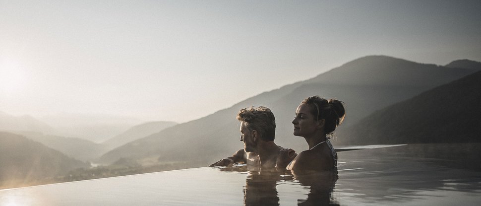 Il nostro hotel a Valdaora tra cielo e terra Coppia rilassata in piscina a sfioro con vista sulle montagne al tramonto
