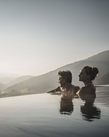 Aktuelle News und Geschichten aus Olang Paar entspannt in Infinity-Pool mit Bergblick bei Sonnenuntergang