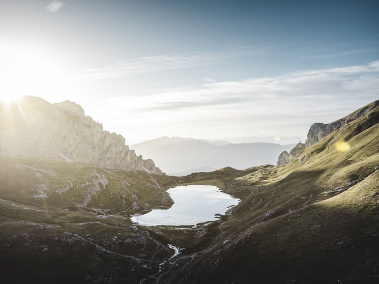 Unser Hotelgutschein: Südtirol im Geschenkformat Sonnenaufgang über einem Bergsee in einer grünen Gebirgslandschaft
