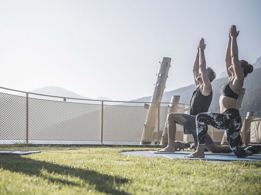 Unser Hotel in Olang zwischen Himmel und Erde Zwei Personen praktizieren Yoga im Freien auf einer Wiese bei Bergblick.
