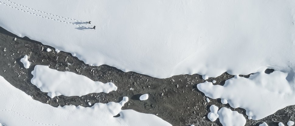 Aktuelle News und Geschichten aus Olang Luftaufnahme von zwei Personen, die durch Schnee am Flussufer wandern