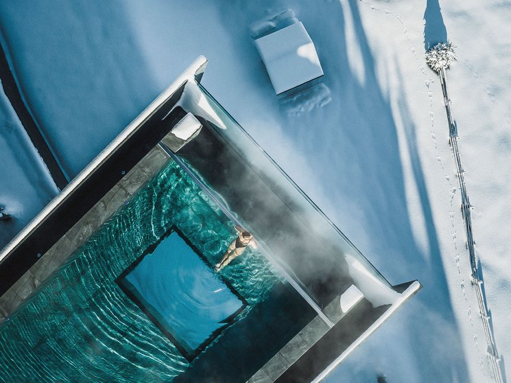 Unser Hotelgutschein: Südtirol im Geschenkformat Person schwimmt in beheiztem Pool umgeben von Schnee und Winterlandschaft