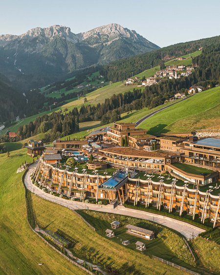 Il nostro hotel a Valdaora tra cielo e terra Hotel di lusso su prato verde con montagne alpine sullo sfondo