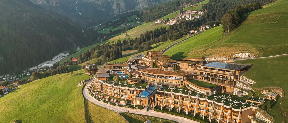 Il nostro hotel a Valdaora tra cielo e terra Hotel di lusso su prato verde con montagne alpine sullo sfondo