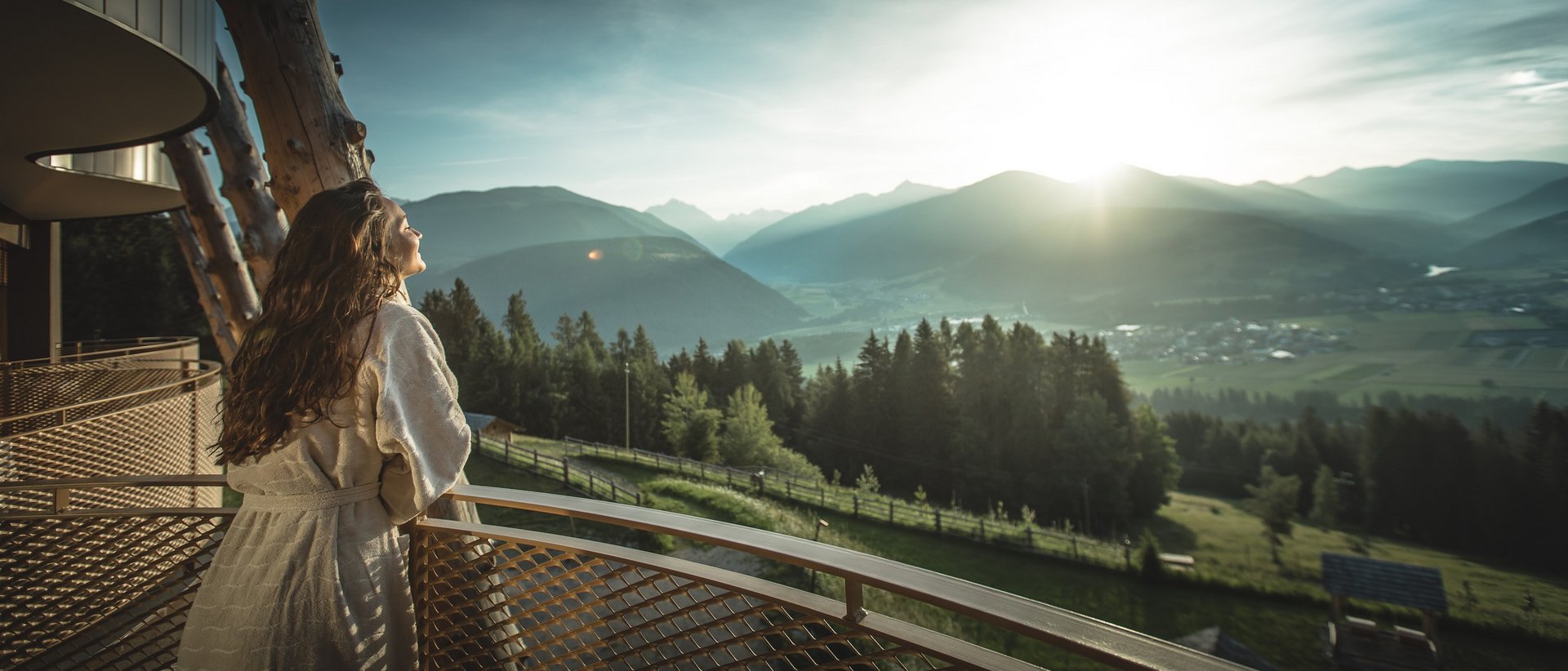 Unser Hotel in Olang zwischen Himmel und Erde Frau in Bademantel genießt Sonnenaufgang über Bergen von einem Balkon aus