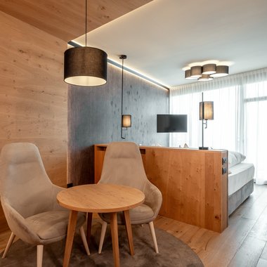 Winterurlaub in der Kronplatz-Region: unglaublich facettenreich Modernes Hotelzimmer mit zwei Stühlen, kleinem Tisch und indirekter Beleuchtung