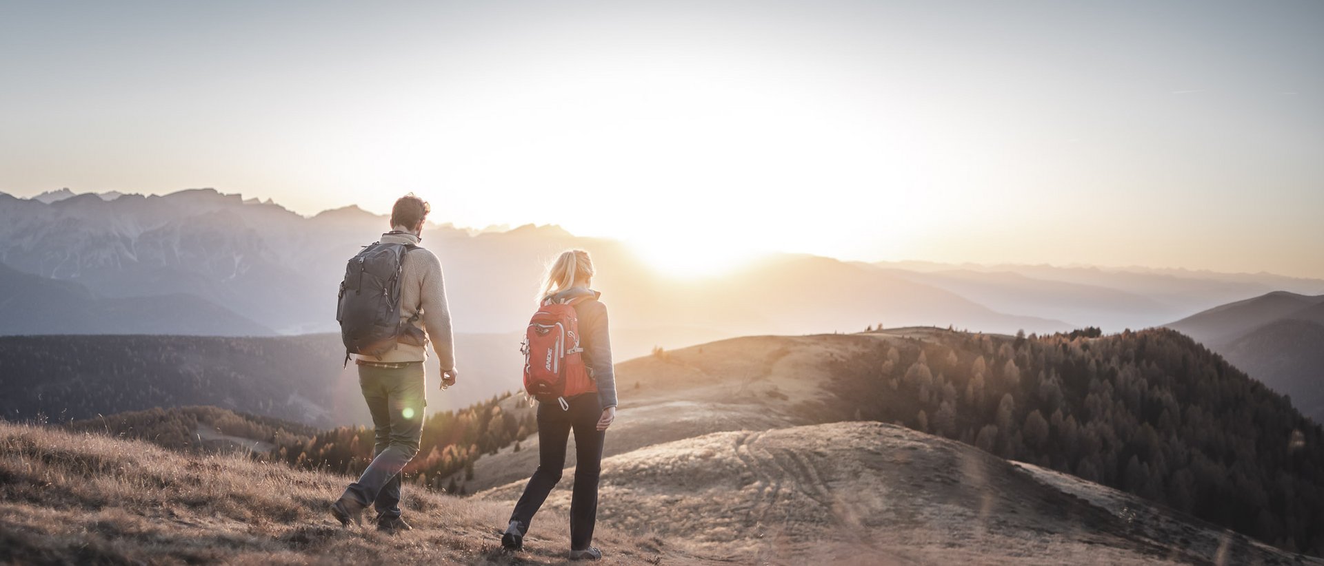 Aktivurlaub in Südtirol: ein Erlebnis Zwei Wanderer mit Rucksäcken gehen bei Sonnenuntergang in den Bergen