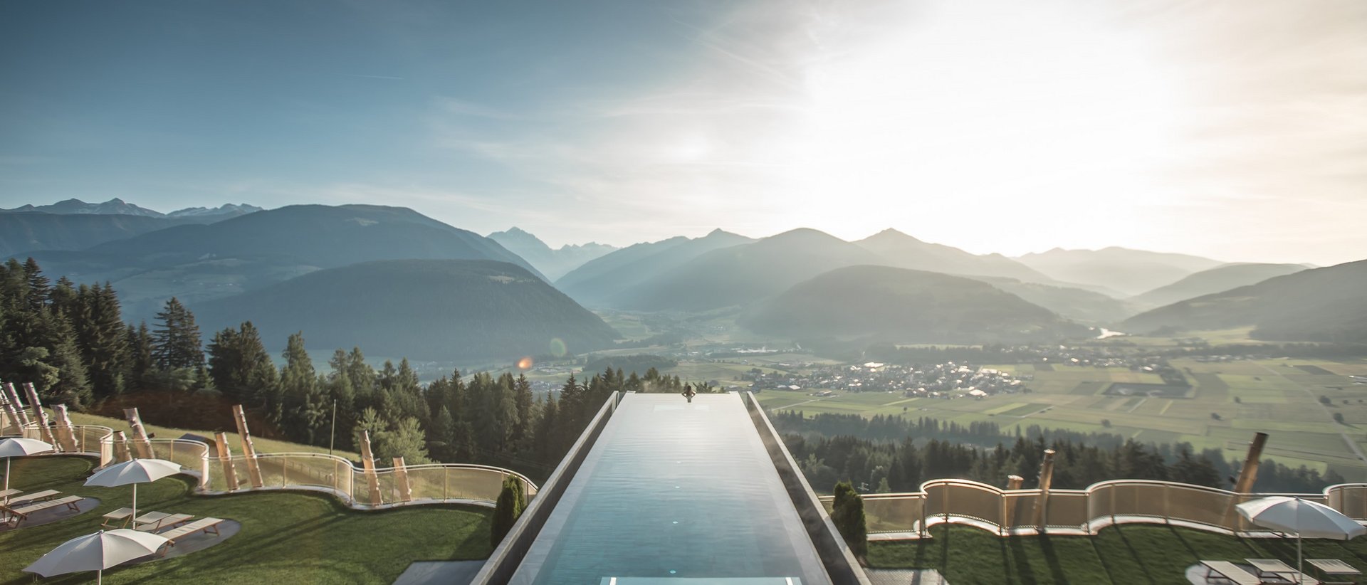 Das Wellnesshotel im Pustertal zum Entspannen Infinity-Pool mit Blick auf Berge und Tal in Sonnenlicht