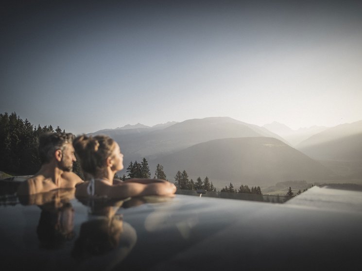 Das Wellnesshotel im Pustertal zum Entspannen Paar entspannt im Außenpool mit Blick auf Berge bei Sonnenuntergang