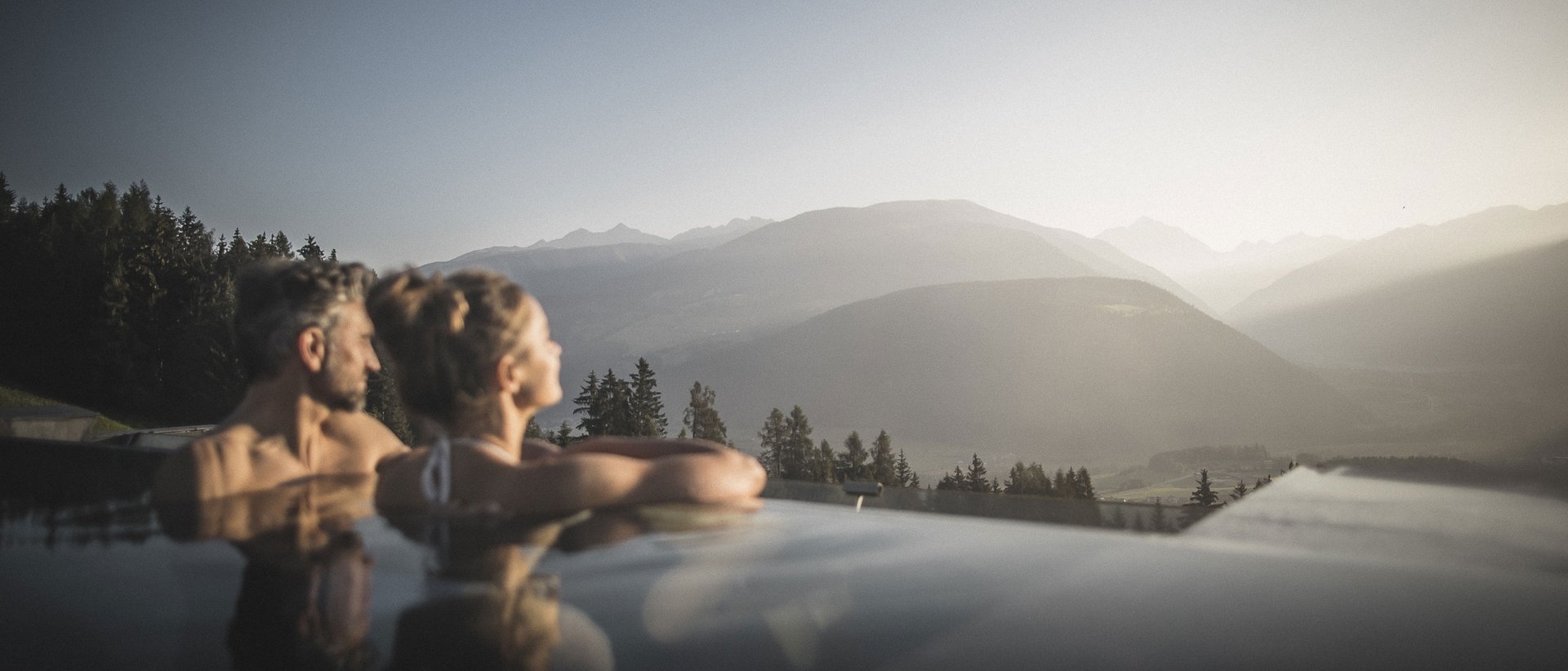 Erholung auf allen Ebenen des Seins Paar entspannt im Außenpool mit Blick auf Berge bei Sonnenuntergang