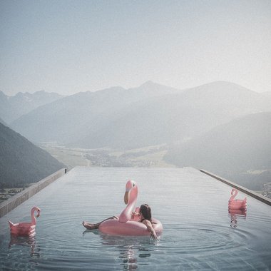 Das Wellnesshotel im Pustertal zum Entspannen Entspannter Mensch auf Flamingo-Schwimmring im Infinity-Pool mit Bergblick