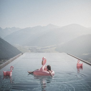 Unser Hotel mit Fitnessstudio in Südtirol Entspannter Mensch auf Flamingo-Schwimmring im Infinity-Pool mit Bergblick