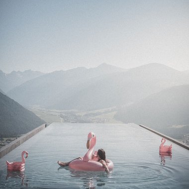 Unsere Sauna, den Kronplatz im Blickfeld Entspannter Mensch auf Flamingo-Schwimmring im Infinity-Pool mit Bergblick