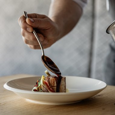 A look at our wine list Chef pouring sauce over a small piece of meat on a white plate