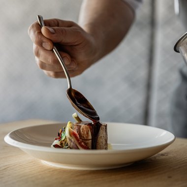 Uno sguardo alla nostra carta dei vini Cuoco versa salsa su un piccolo pezzo di carne su un piatto bianco