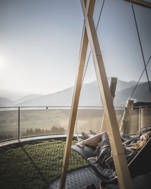 Unser Hotelgutschein: Südtirol im Geschenkformat Person liegt entspannt auf einer Hängematte mit Bergblick