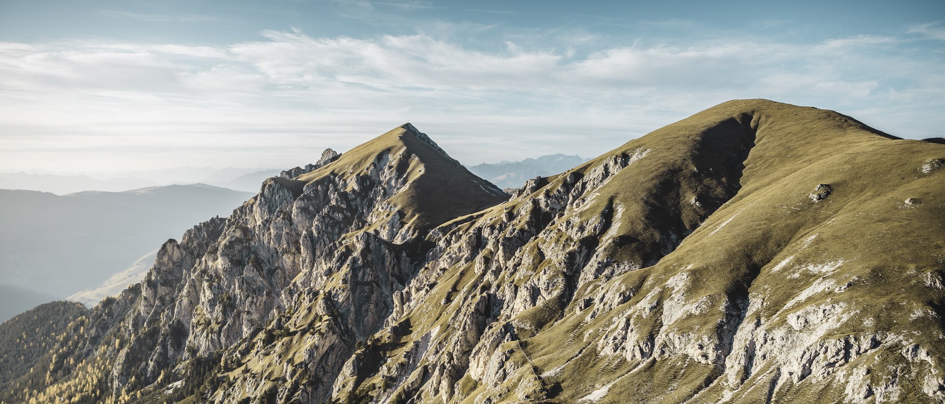 Aktivurlaub in Südtirol: ein Erlebnis Gebirgskamm mit steilen Felsen und bewaldeten Tälern bei klarem Himmel